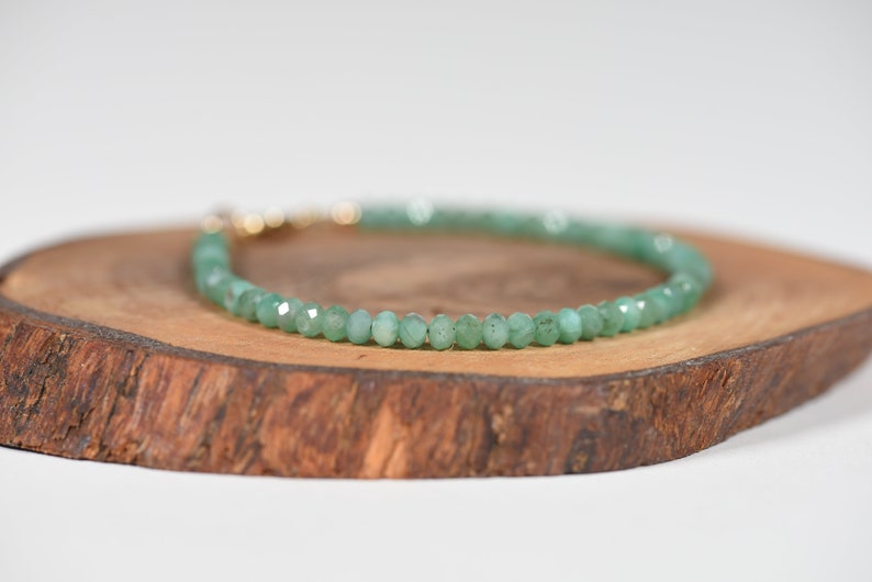 Op de afbeelding: Een groene edelsteen armband met een gouden sluiting. De armband is gemaakt van kleine, ronde kralen en wordt getoond op een houten oppervlak.
