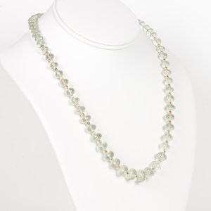 May include: A green crystal bead necklace with gold accents. The necklace is displayed on a white mannequin bust.