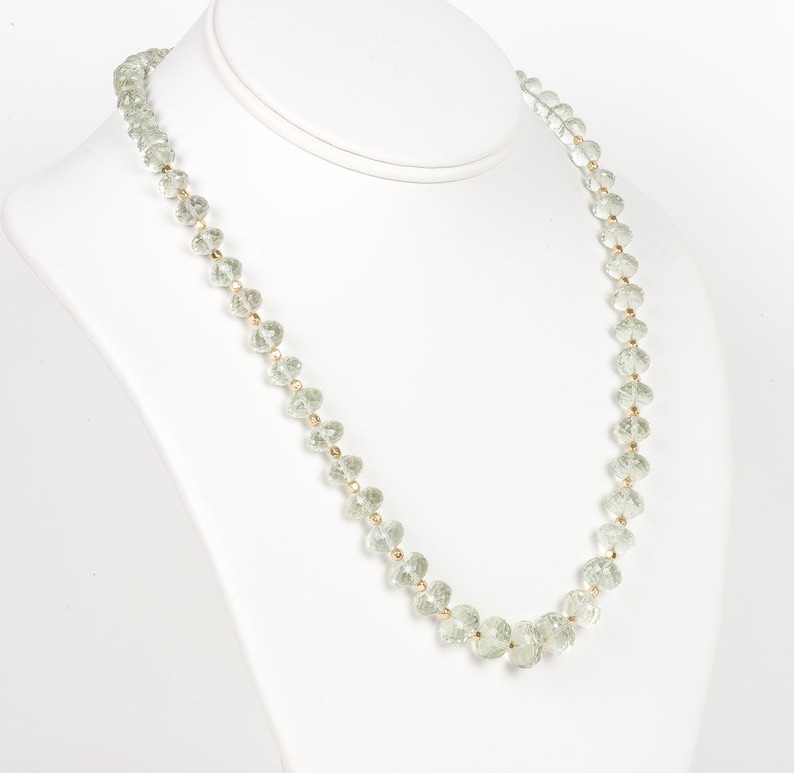 May include: A green crystal bead necklace with gold accents. The necklace is displayed on a white mannequin bust.