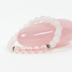 Op de afbeelding: Een armband van witte en roze edelstenen met zilveren kralen. De armband ligt op een roze rozenkwarts steen.