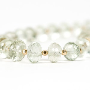 May include: A close-up of a green gemstone necklace with gold beads. The necklace is made of faceted, round gemstones and is strung on a gold chain.
