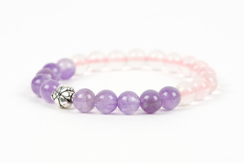 May include: A purple and pink beaded bracelet with a silver charm. The bracelet is made with amethyst and rose quartz beads.
