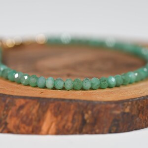 Op de afbeelding: Een groene edelsteen armband met een gouden sluiting. De armband is gemaakt van kleine, gefacetteerde kralen en ligt op een houten oppervlak.
