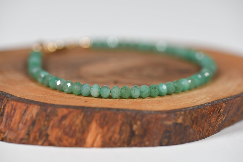 Op de afbeelding: Een groene edelsteen armband met een gouden sluiting. De armband is gemaakt van kleine, gefacetteerde kralen en ligt op een houten oppervlak.