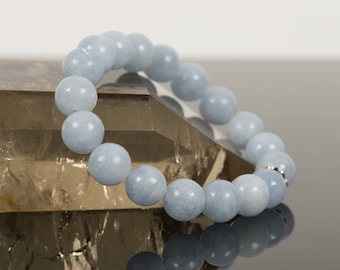 May include: A light blue gemstone bracelet with round beads. The bracelet is resting on a clear crystal.