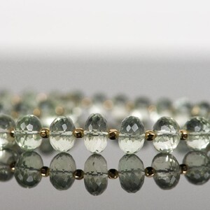 May include: A strand of light green gemstone beads with gold accents. The beads are faceted and have a reflective surface.