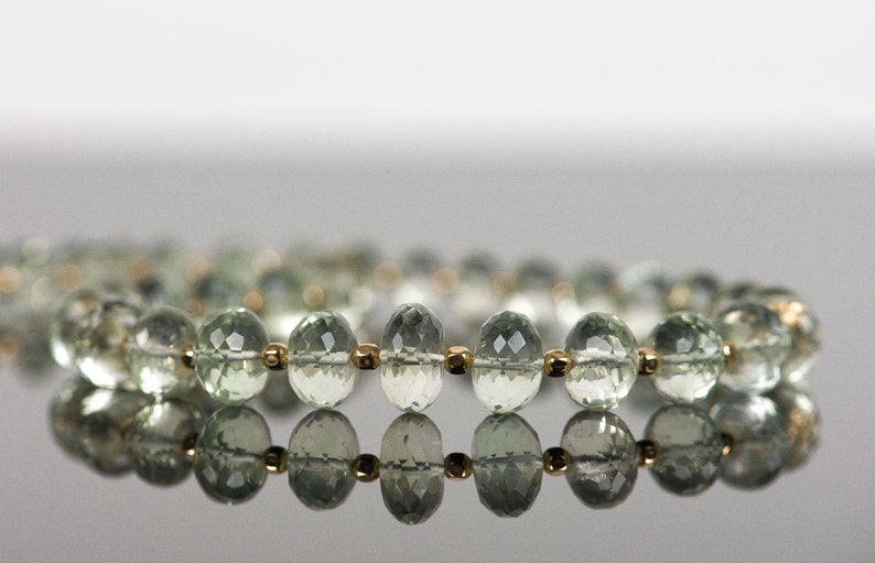 May include: A strand of light green gemstone beads with gold accents. The beads are faceted and have a reflective surface.