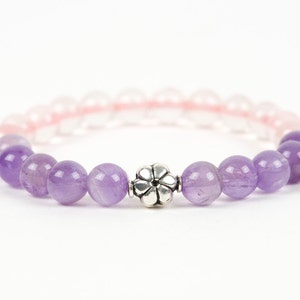 May include: A purple and pink gemstone bracelet with a silver flower charm. The bracelet is made with amethyst and rose quartz beads.