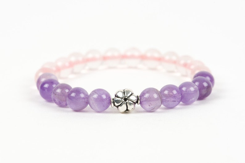 May include: A purple and pink gemstone bracelet with a silver flower charm. The bracelet is made with amethyst and rose quartz beads.