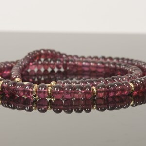 Puede incluir: Un collar de m&uacute;ltiples hilos hecho de peque&ntilde;as cuentas redondas de color p&uacute;rpura con detalles dorados.