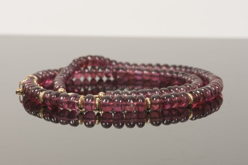Puede incluir: Un collar de m&uacute;ltiples hilos hecho de peque&ntilde;as cuentas redondas de color p&uacute;rpura con detalles dorados.