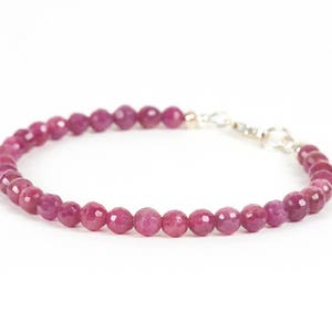 Puede incluir: Un brazalete de piedras preciosas rosas con un cierre plateado. El brazalete está hecho de pequeñas cuentas redondas.