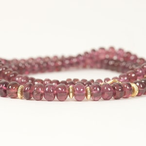Puede incluir: Un collar de piedras preciosas rosas con cuentas doradas. El collar est&aacute; hecho de piedras preciosas redondas y facetadas y est&aacute; enhebrado en una cadena dorada.