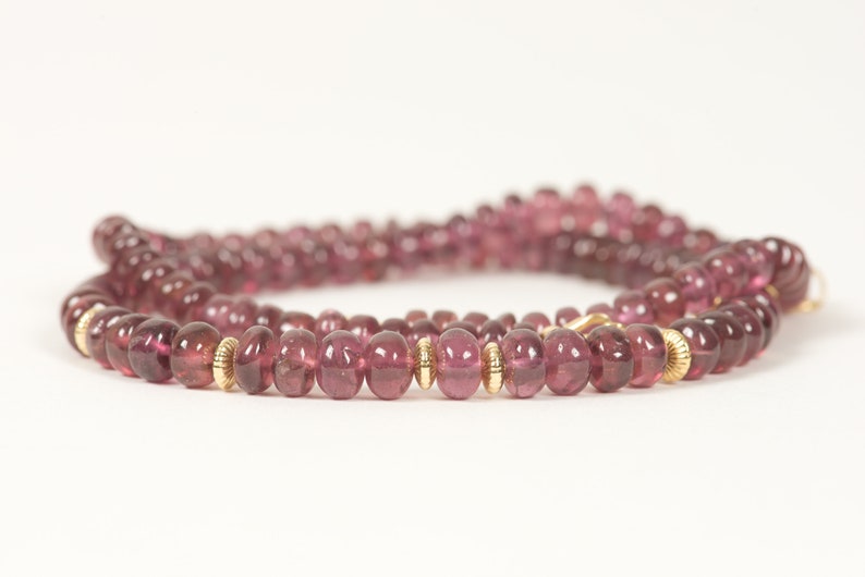 Puede incluir: Un collar de piedras preciosas rosas con cuentas doradas. El collar est&aacute; hecho de piedras preciosas redondas y facetadas y est&aacute; enhebrado en una cadena dorada.