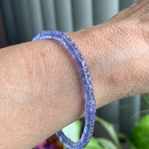 May include: A purple gemstone bracelet made of small, faceted beads. The bracelet is worn on a person's wrist.