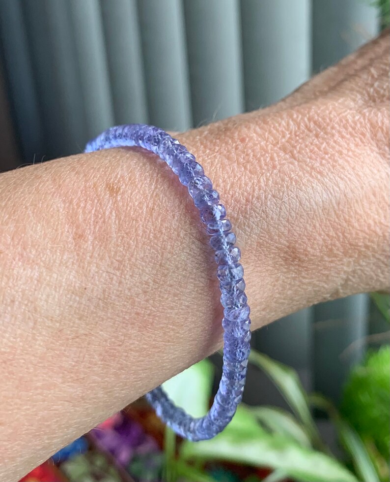 May include: A purple gemstone bracelet made of small, faceted beads. The bracelet is worn on a person's wrist.