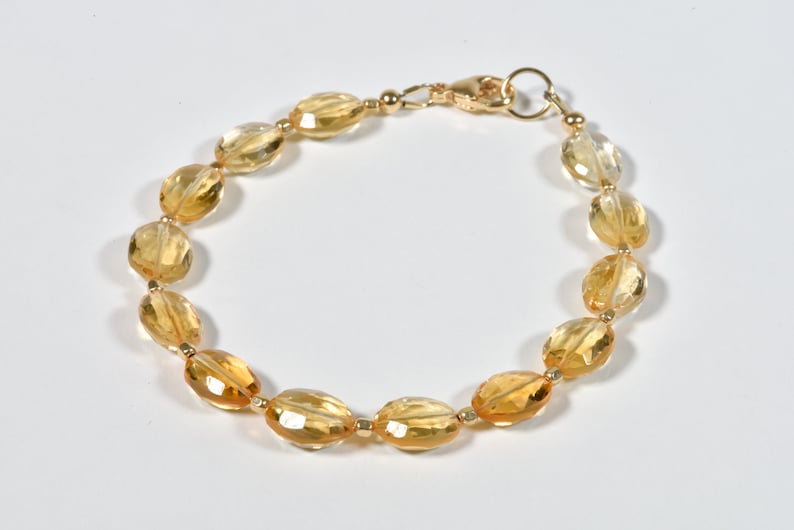 May include: A gold bracelet with oval-shaped, faceted citrine gemstones. The bracelet has a lobster claw clasp.