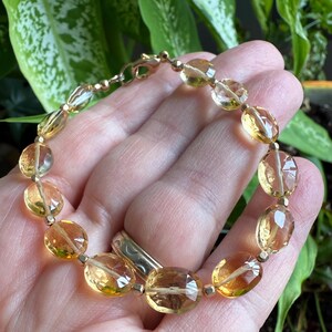 May include: A gold bracelet with oval-shaped, faceted citrine gemstones. The bracelet has a lobster clasp closure.
