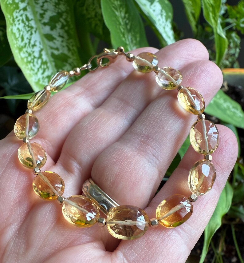 May include: A gold bracelet with oval-shaped, faceted citrine gemstones. The bracelet has a lobster clasp closure.