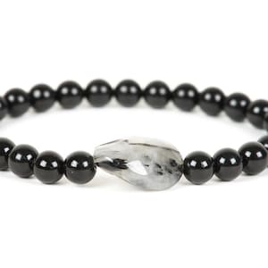May include: A black beaded bracelet with a single clear and grey gemstone charm.