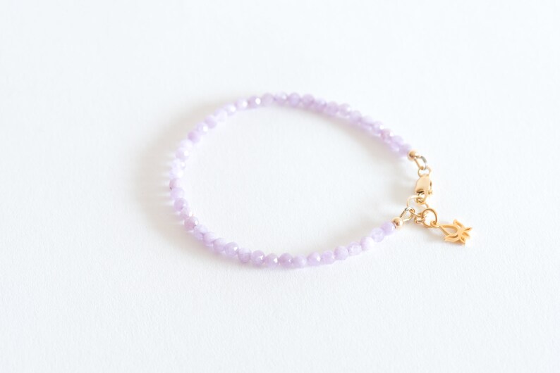 Peut inclure: Un bracelet d&eacute;licat compos&eacute; de petites perles de couleur lilas clair et d'un fermoir en or avec un pendentif en forme de fleur de lotus.