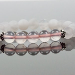 Op de afbeelding: Een armband van witte en roze edelstenen met zilveren accenten. De armband is gemaakt van ronde kralen en heeft een eenvoudig ontwerp.