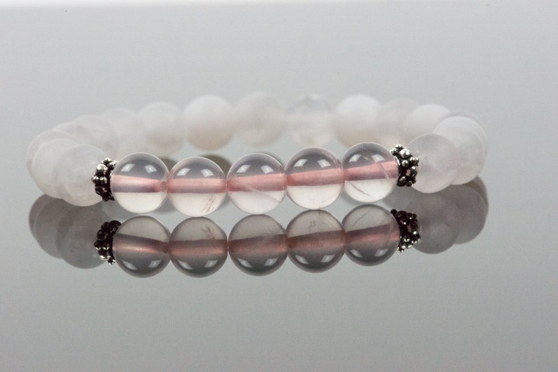 Op de afbeelding: Een armband van witte en roze edelstenen met zilveren accenten. De armband is gemaakt van ronde kralen en heeft een eenvoudig ontwerp.