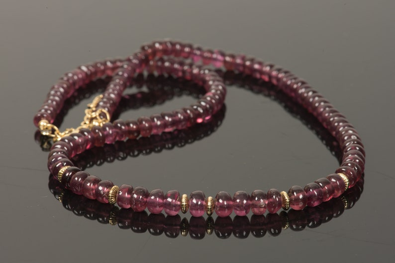 Puede incluir: Un collar largo hecho de peque&ntilde;as cuentas redondas de color p&uacute;rpura con detalles dorados. El collar est&aacute; hecho de piedras preciosas naturales y es una hermosa pieza de joyer&iacute;a.
