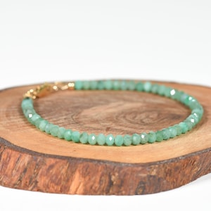 Op de afbeelding: Een armband van groene edelstenen met een gouden sluiting. De armband is gemaakt van kleine, gefacetteerde kralen en wordt getoond op een houten oppervlak.
