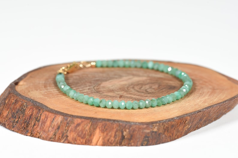 Op de afbeelding: Een armband van groene edelstenen met een gouden sluiting. De armband is gemaakt van kleine, gefacetteerde kralen en wordt getoond op een houten oppervlak.