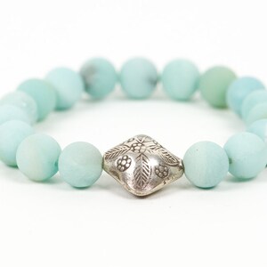 May include: A light blue beaded bracelet with a silver charm featuring a floral design.
