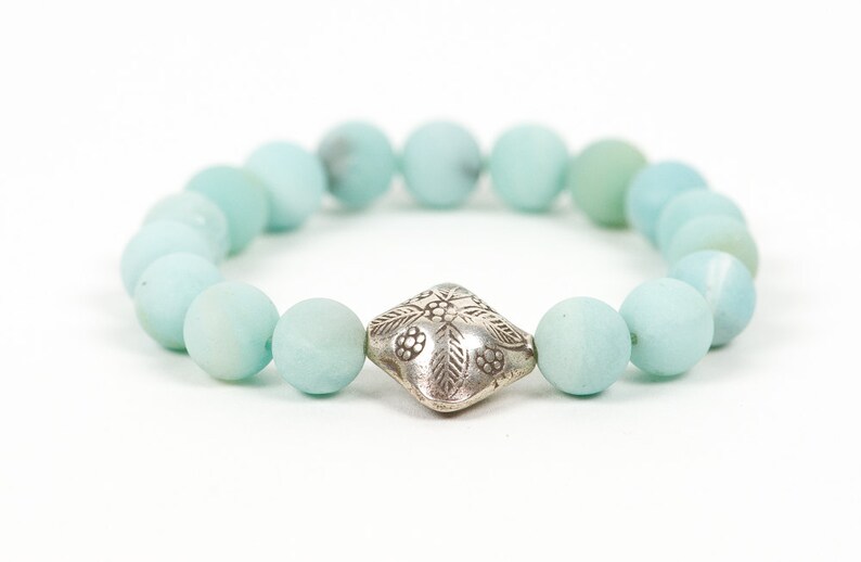May include: A light blue beaded bracelet with a silver charm featuring a floral design.