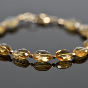 May include: A gold bracelet with oval-shaped, faceted, topaz gemstones. The bracelet is made of gold beads and has a clasp closure.