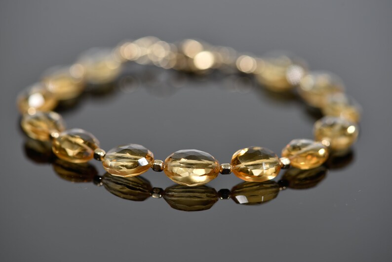 May include: A gold bracelet with oval-shaped, faceted, topaz gemstones. The bracelet is made of gold beads and has a clasp closure.