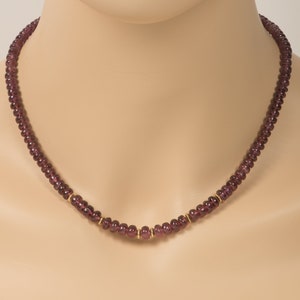 Puede incluir: Un collar de piedras preciosas de color p&uacute;rpura con detalles dorados. El collar est&aacute; hecho de peque&ntilde;as cuentas redondas y mide aproximadamente 45 cent&iacute;metros de largo.