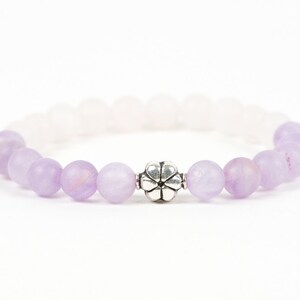 May include: A purple and white beaded bracelet with a silver flower charm.