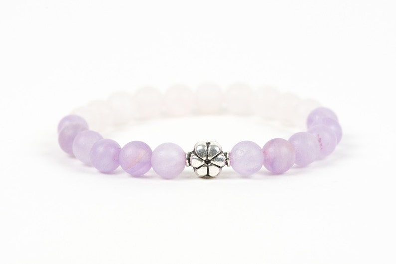 May include: A purple and white beaded bracelet with a silver flower charm.