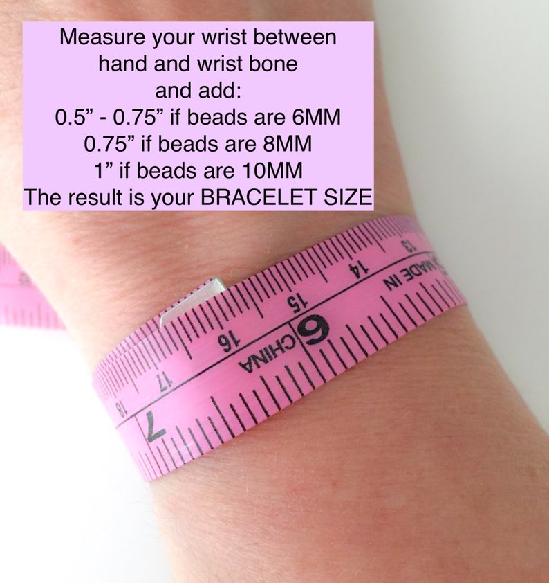 Op de afbeelding: Een roze meetlint gewikkeld om een pols met instructies om de pols te meten tussen de hand en het polsbot en 0,5 inch toe te voegen als de kralen 6 mm zijn, 0,75 inch als de kralen 8 mm zijn of 1 inch als de kralen 10 mm zijn. Het resultaat is de armbandmaat.