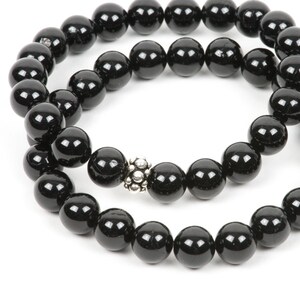 May include: A black beaded bracelet with a silver charm. The bracelet is made of round beads and is double-stranded.