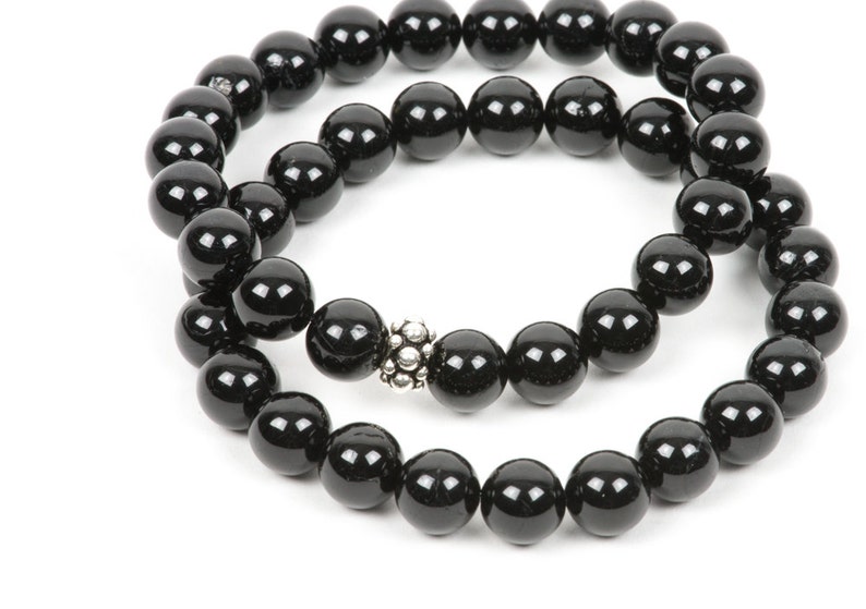 May include: A black beaded bracelet with a silver charm. The bracelet is made of round beads and is double-stranded.