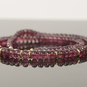 Puede incluir: Un collar largo hecho de peque&ntilde;as cuentas redondas de color rosa oscuro con detalles dorados.