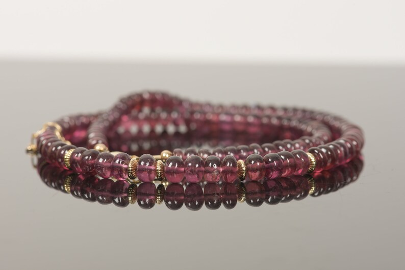 Puede incluir: Un collar largo hecho de peque&ntilde;as cuentas redondas de color rosa oscuro con detalles dorados.