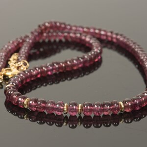 Puede incluir: Un collar de piedras preciosas rosas con detalles dorados. El collar est&aacute; hecho de cuentas redondas y tiene un cierre.