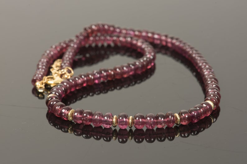 Puede incluir: Un collar de piedras preciosas rosas con detalles dorados. El collar est&aacute; hecho de cuentas redondas y tiene un cierre.