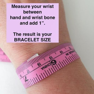 May include: Pink measuring tape wrapped around a wrist with instructions to measure the wrist between the hand and wrist bone and add 1 inch. The text "The result is your BRACELET SIZE" is also included.