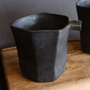May include: A black ceramic jug with a distinctive octagonal shape and a spout. The jug has a matt finish and a subtle texture.