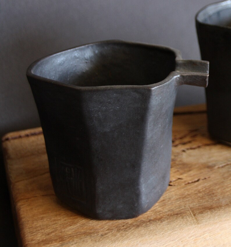 May include: A black ceramic jug with a distinctive octagonal shape and a spout. The jug has a matt finish and a subtle texture.