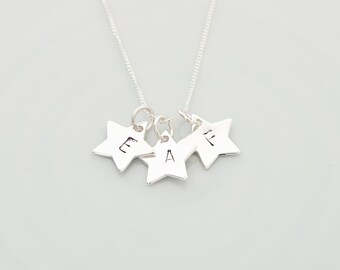 May include: A silver necklace with three star-shaped charms, each with a letter engraved on it. The letters are E, A, and F.