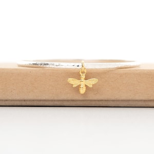 May include: A silver bangle bracelet with a hammered texture and a gold bee charm.