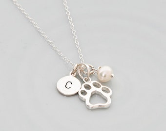 May include: Silver necklace with a paw print charm, a small pearl charm, and a round charm with the letter "C" engraved on it.